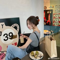 a woman sitting at a table in front of a sign holding a drink and looking at her cell phone