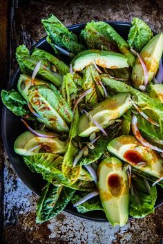 lettuce and avocado salad with red onion dressing on a black plate