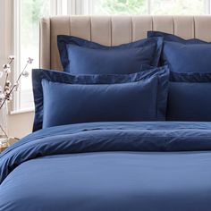 a bed with blue sheets and pillows in front of a window