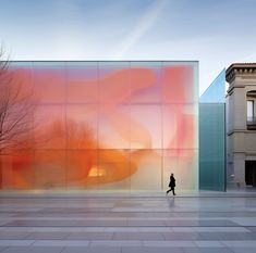 a person walking in front of a building with an orange and pink painting on it