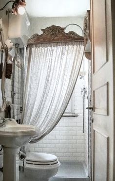 a white toilet sitting next to a bath tub under a bathroom window covered in sheer curtains