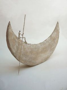 a sculpture of a man sitting on top of a half moon with a stick in it