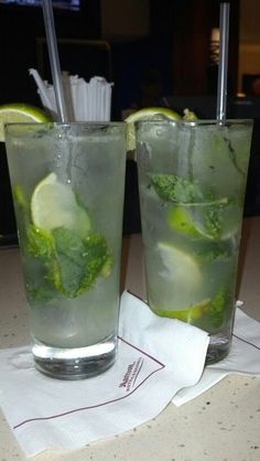 two glasses filled with ice and limes on top of a table next to each other