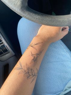 a person with a flower tattoo on their arm sitting in a car and holding the steering wheel