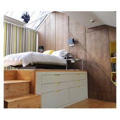 a bed sitting on top of a wooden floor next to a white dresser under a skylight