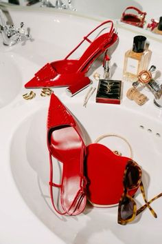 a pair of red high heeled shoes sitting on top of a sink next to sunglasses