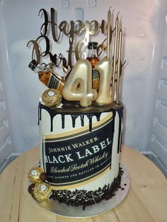 a black and white birthday cake with gold decorations on the top is decorated with liquor bottles