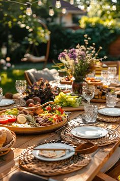 a wooden table topped with lots of plates and bowls filled with food next to trees