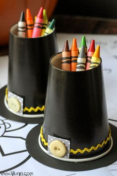 two black cups with crayons in them sitting on top of a table