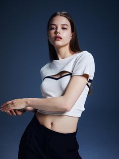 a young woman poses in front of a blue background wearing a white shirt and black pants