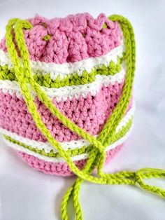 a crocheted pink and white bag with green handles on a white tablecloth