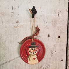 a red plate with a snowman on it hanging from a rope against a white wall