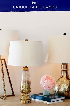 three lamps are sitting on a table next to books and a vase with flowers in it