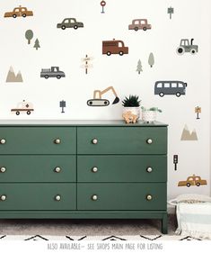 a green dresser sitting in front of a wall with cars and trucks painted on it