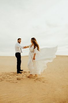 a man and woman standing in the sand holding hands