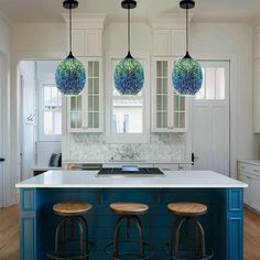 three lights hanging over a kitchen island with stools in front of the counter top