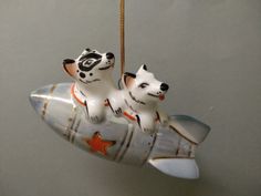 two white dogs are sitting on top of a rocket ship ornament hanging from a rope