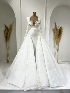 a white wedding gown with long sleeves and a train on display in front of a mannequin