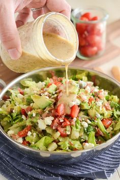 someone pouring dressing into a salad in a pan