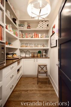 a kitchen with white cabinets and shelves filled with food on top of wooden flooring