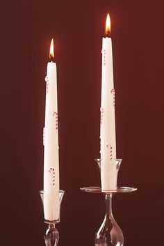 two white candles sitting on top of each other in front of a red background,