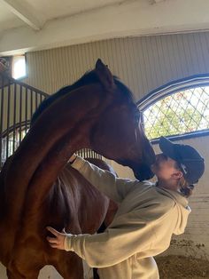 a man standing next to a brown horse inside of a stable with another person petting the horse