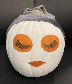 a white pumpkin with orange eyes and lashes painted on it's face, sitting on a black surface