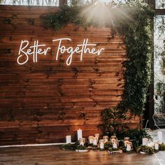 a wooden wall with candles and greenery on the floor next to it that says better together