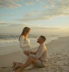 a pregnant couple sitting on the beach at sunset