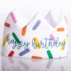 a white birthday crown with colorful confetti on it's side and the words happy birthday written in blue