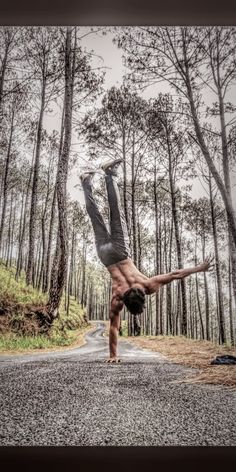 a man doing a handstand on the side of a road in front of trees