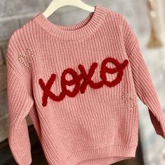 a pink sweater with the word exox on it hanging from a clothes hanger