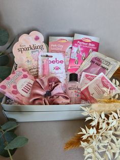 a pink gift box filled with lots of beauty products and personal care items next to some flowers