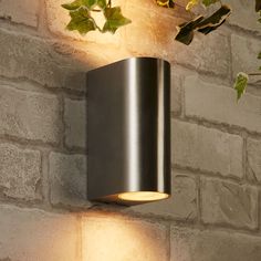 a modern outdoor light mounted on the side of a brick wall next to a plant