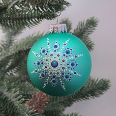 a green christmas ornament hanging from a pine tree with snowflakes on it