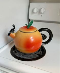 an orange tea pot sitting on top of a stove