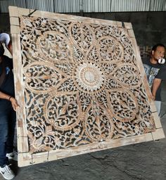 two men are standing next to a large wooden piece that has been carved into the shape of a flower