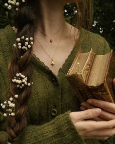 a woman with braids holding a book in her hands and wearing a flower crown