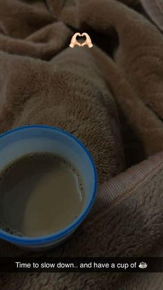 a cup of coffee sitting on top of a bed next to a brown blanket with the words time to slow down and have a cup of coffee