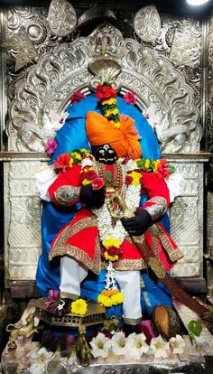 a statue of the hindu god person sitting on a throne with flowers around his feet