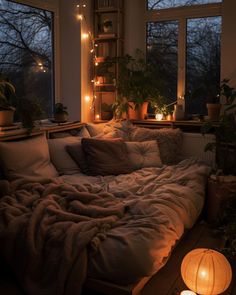 an unmade bed in front of two windows with candles on the window sill