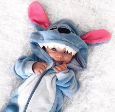 a baby dressed in a blue and white animal costume laying on top of a bed