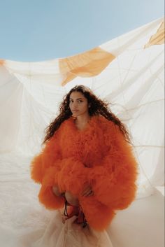 a woman in an orange dress sitting on the ground with her arms around her body