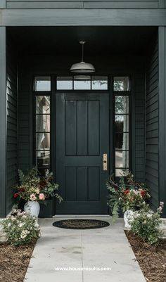 a black front door with two white vases filled with flowers and greenery on the side