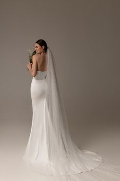 a woman in a wedding dress holding a flower and looking at the back of her gown