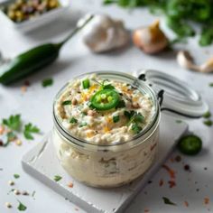 a small jar filled with food sitting on top of a white table next to green peppers