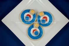 three decorated cookies sitting on top of a white square plate with blue and red designs