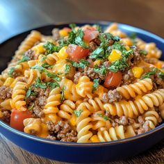 a blue bowl filled with pasta and meat topped with parsley on top of a wooden table