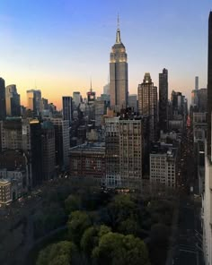 the city skyline is lit up at night with skyscrapers in the distance and trees on either side