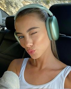 a young woman wearing headphones in the back seat of a car, making a funny face